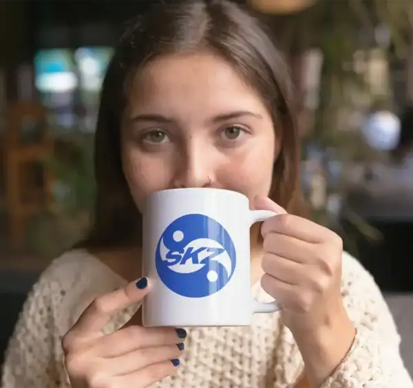 Skz kpop merch, girl holding a white mug with blue SKZ logo in a cozy café setting.