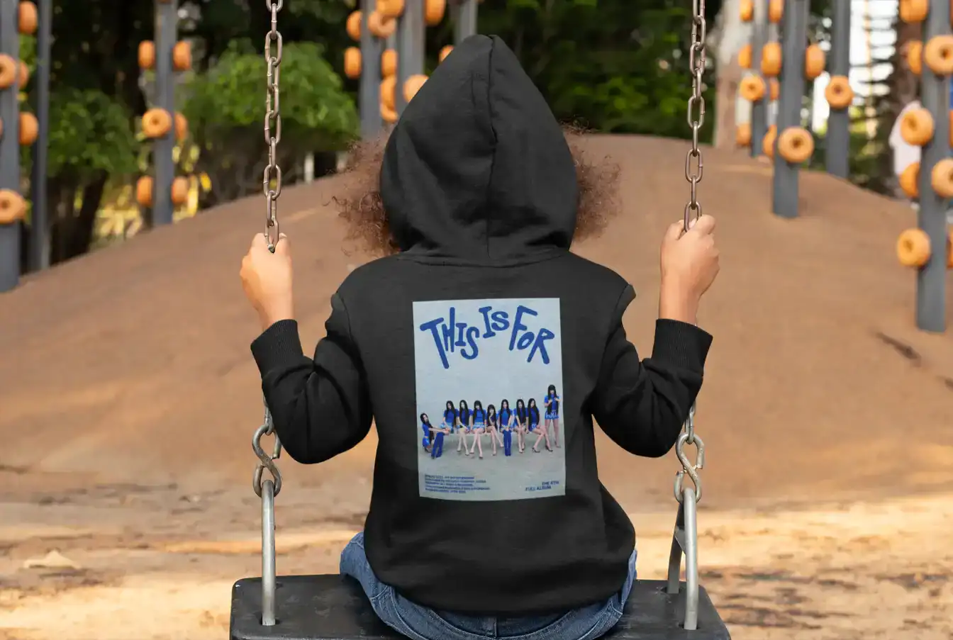 Vibrant K-pop group poster on a black hoodie worn by a child sitting on a swing.