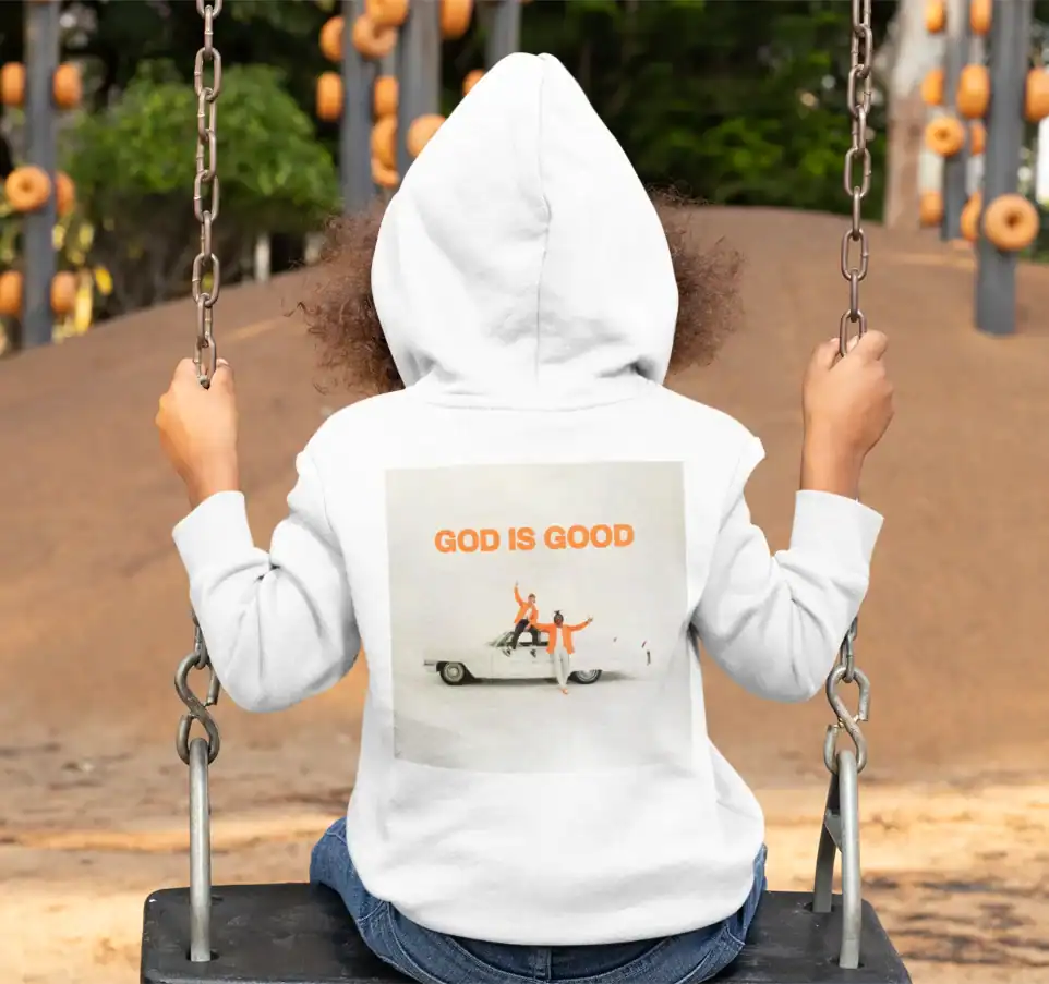 GOD IS GOOD hoodie on a child sitting on a swing at the park.